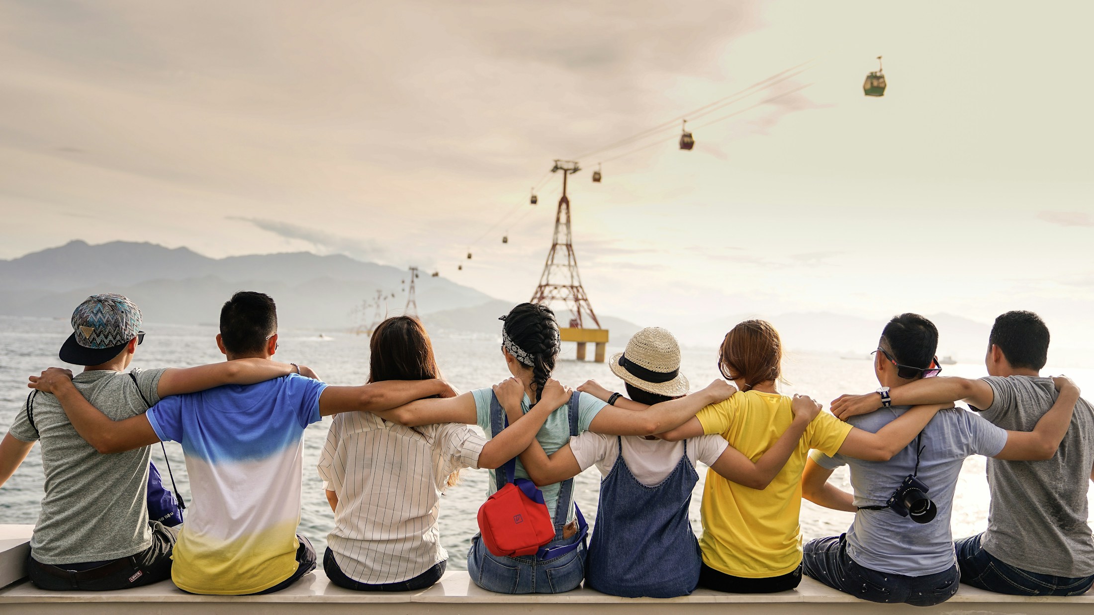 Friends sitting together by the waterfront with their arms around each other